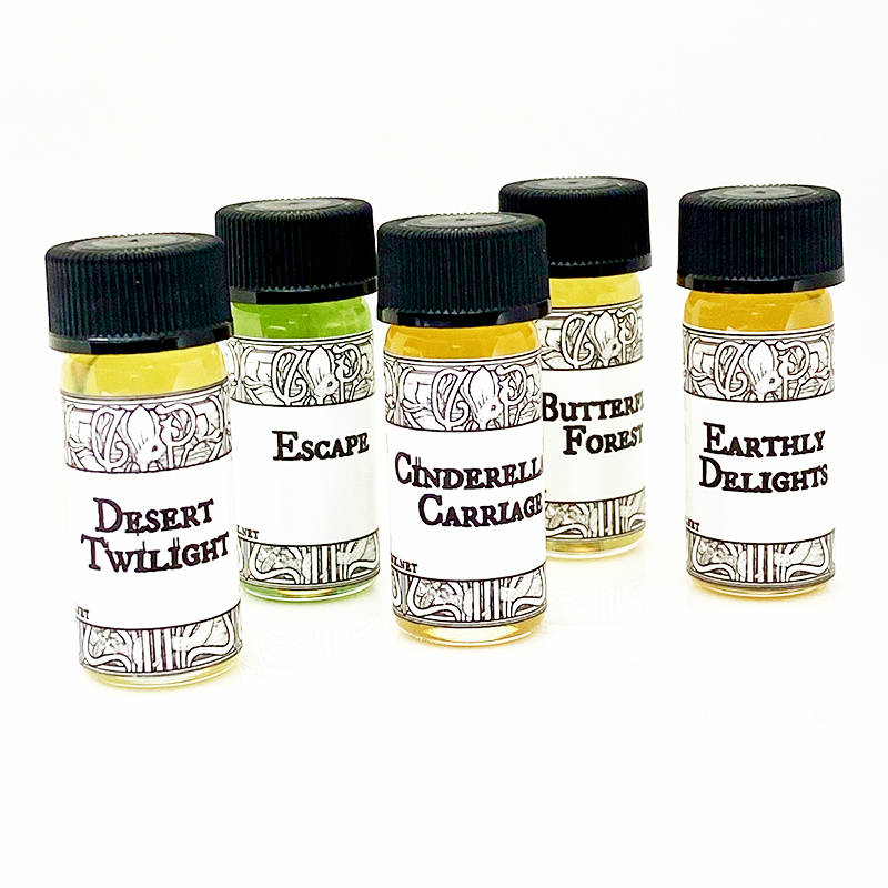 A set of five small, clear glass vials with black caps and labels, containing perfume oils. 