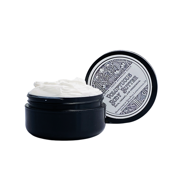 A jar of body butter with its lid off, showing a creamy white product inside. The jar is placed on a surface with a decorative lid.
